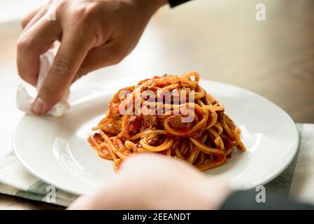 Mano dello chef strofinare il piatto di spaghetti bolognese dopo la placcatura, preparandosi per servire Foto Stock