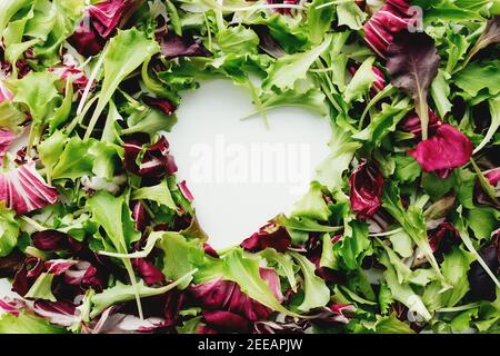 Forma del cuore da foglie di insalata verde e viola mescolano lo sfondo. Tavola bianca. Foto di alta qualità Foto Stock