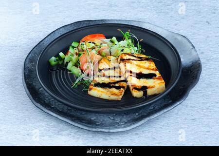 Fette di alloumi alla griglia con insalata di verdure, pomodori e cetrioli Foto Stock