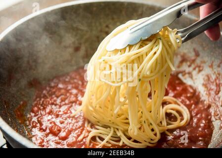 Gli spaghetti italiani cotti vengono messi in padella con il fuoco salsa bolognese Foto Stock