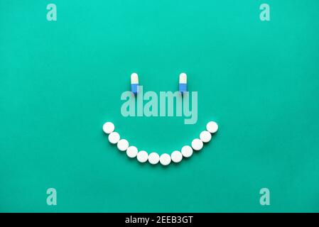 Capsule mediche e pillole disposte in felice sorriso faccia sopra sfondo verde Foto Stock