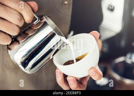 Barista professionista che versa il latte in cottura a vapore in una tazza di caffè e prepara il latte arte Foto Stock