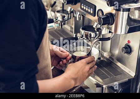 Barista che prepara il latte nel caraffa con la macchina per il caffè per fare la latte art in caffetteria Foto Stock