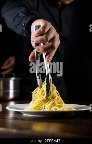 La tradizionale pasta italiana di spaghetti viene cucinata e preparata dallo chef al tavolo in cucina Foto Stock