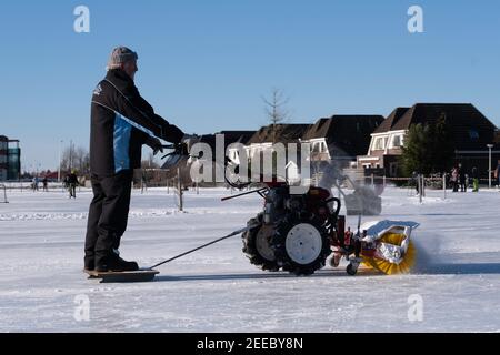 L'uomo pulisce la pista di ghiaccio nella neve d'inverno con una spazzatrice e un spazzaneve. Può essere tirato su una slitta. Foto Stock