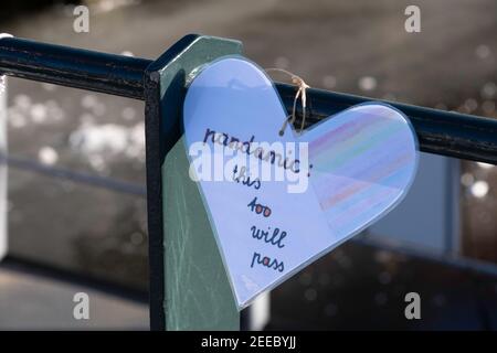 Il cuore di carta plastificata con il testo scritto a mano 'Pandamic: This too will pass' pende dalla ringhiera di un ponte a Lemmer, Paesi Bassi Foto Stock