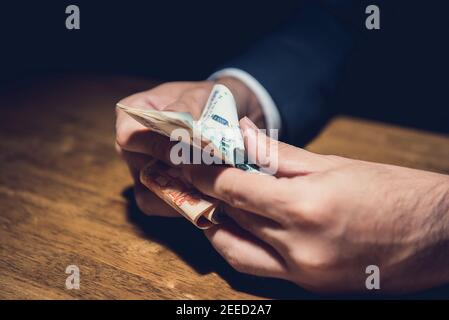 Uomo d'affari che conta denaro, valuta rubla russa, al tavolo in camera privata oscura - concetti di venalità e corruzione Foto Stock
