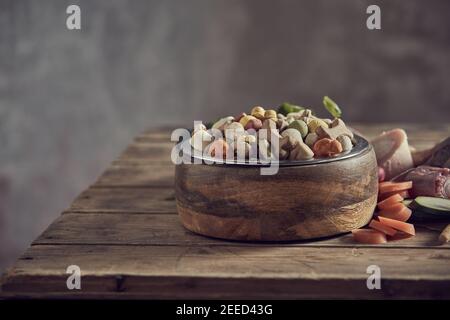 Ciotola di sani biscotti secchi del cane o pellet con ingredienti vegetali freschi assortiti e ossa carnose su un rustico tabella Foto Stock