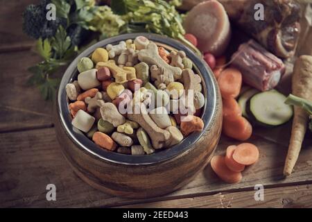 Ciotola piena di sano equilibrato cibo per cani secchi per il vostro animali domestici circondati da ingredienti freschi, tra cui una varietà di verdure e ossa carnose visto Foto Stock