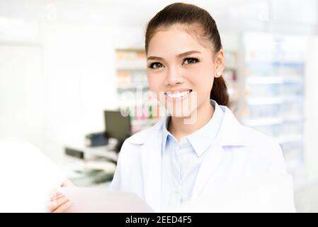 Sorridente giovane donna asiatica farmacista in camice bianco guardando a macchina fotografica mentre si lavora in farmacia (farmacia o farmacia) Foto Stock