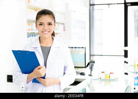 Sorridente bella giovane donna asiatica farmacista in camice bianco al lavoro in farmacia (farmacia o farmacia) Foto Stock