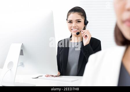 Sorridente bella donna asiatica telemarketing agente di servizio di cliente che lavora dentro ufficio call center Foto Stock