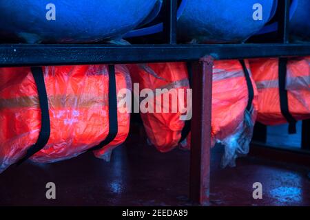 Giacca rossa sotto la sedia di plastica blu. Equipaggiamento di sicurezza per i traghetti. Apparecchio salvavita in cabina. Norme di sicurezza per il trasporto di passeggeri Foto Stock