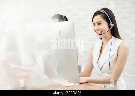 Sorridente bella donna asiatica telemarketing agente di servizio di cliente che lavora dentro ufficio call center Foto Stock