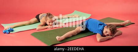 Carino bambini in abbigliamento sportivo che guarda via e sorridente mentre fa esercizi di stretching su stuoie per yoga Foto Stock