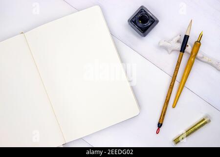 Pagina vuota del libro di schizzo con gli strumenti di calligrafia. Foto vista dall'alto del notebook su sfondo bianco. Disposizione piatta minima con strumenti di disegno e glitter oro. WH Foto Stock