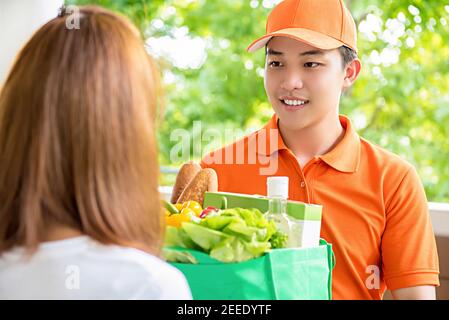 Uomo asiatico che consegna il cibo a una donna a casa - concetto di servizio di acquisto di generi alimentari online Foto Stock