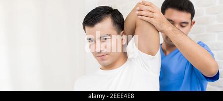 Allenamento terapeuta esercizio di riabilitazione, stretching tricep overhead, per il paziente maschile in ospedale - concetto di terapia fisica, banner panoramico Foto Stock