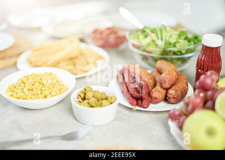Primo piano della colazione in stile latino con mais, olive, insalata e carne sul luminoso tavolo da cucina bianco. Mattina, idee per la colazione. Messa a fuoco selettiva Foto Stock