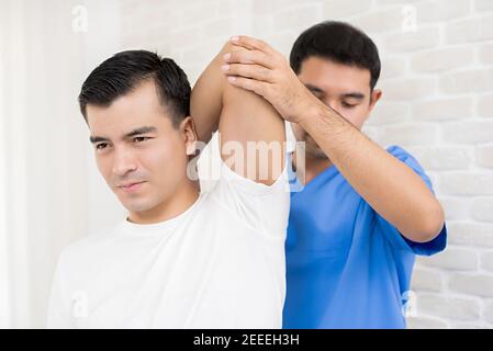 Terapeuta formazione esercizio di riabilitazione, overhead tricep stretching, per il paziente maschile in ospedale - concetto di terapia fisica Foto Stock