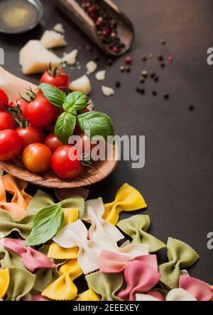 Pasta italiana tricolore FARFALLE con parmigiano e pomodori, sale e pepe con olio su fondo marrone. Vista dall'alto Foto Stock