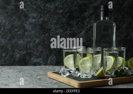 Tavola con bottiglia e colpi di vodka con lime sopra tabella grigia Foto Stock