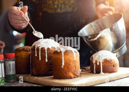 Donna anziana cucina tradizionale Europa orientale Russia e ucraina Pasqua kulich torta decorato con zucchero a velo dolce su tavolo di legno mattina Foto Stock