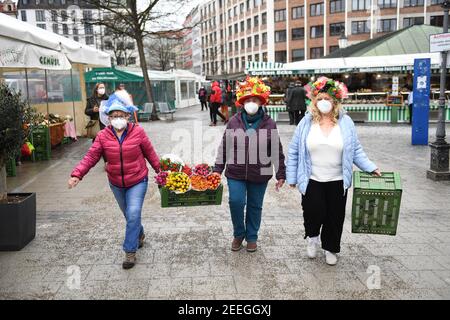 Monaco, Germania. 16 Feb 2021. Le donne del mercato Annemarie Doll (l-r), Erika Schuster e Cristl Lang camminano attraverso il Viktualienmarkt con le casse di frutta il martedì di Shrove. La danza tradizionale delle donne di mercato non si svolge quest'anno a causa della pandemia di Corona. Credit: Felix Hörhager/dpa/Alamy Live News Foto Stock