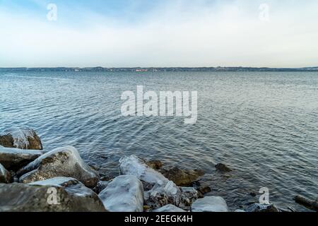 Tinch buchi nella luce del mattino in inverno freddo. Riva del lago di Costanza con sculture naturali di ghiaccio. Spiaggia tedesca con Lindau in background Foto Stock