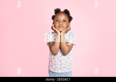 African American bambina nera ragazza sorridente e guardando la macchina fotografica su sfondo rosa, in piedi appoggiandosi il suo viso sulle mani Foto Stock