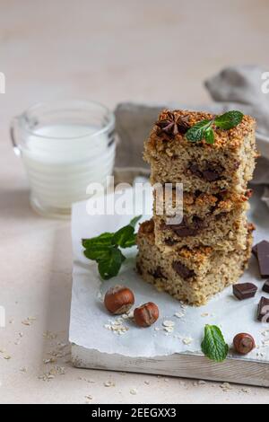 Quadrati di farinata d'avena con cioccolato e una tazza di latte, fondo di cemento chiaro. Dieta bar. Panetteria sana per colazione o dessert. Messa a fuoco selettiva. Foto Stock