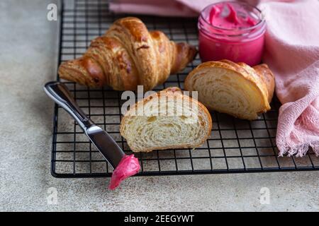 Croissant freschi croccanti con miele rosa su griglia in metallo nero, fondo in cemento. Messa a fuoco selettiva. Foto Stock