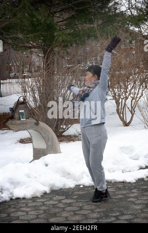 In una fredda mattinata invernale, una donna cinese americana balla ed esercizi di musica dal suo iphone. A Flushing, Queens, New York City. Foto Stock