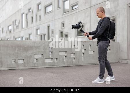 concetto di filmmaking, hobby e creatività - ritratto a tutta lunghezza di un videografo professionista che scatta video utilizzando una moderna fotocamera dslr su un cardanico a 3 assi Foto Stock