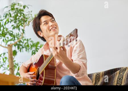 Uomo giapponese che suona la chitarra a casa Foto Stock