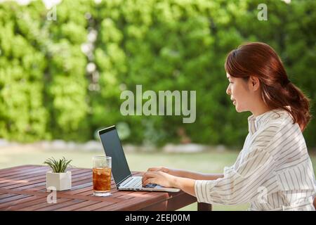 Donna giapponese che lavora con il computer portatile in giardino Foto Stock