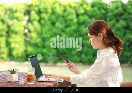 Donna giapponese che lavora con il computer portatile in giardino Foto Stock