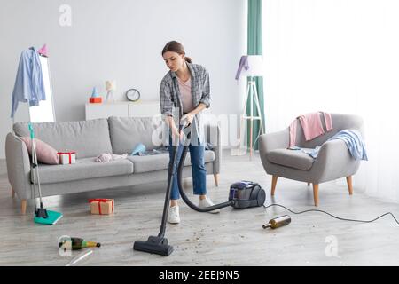 Infelice giovane donna che vacuuming appartamento disordinato dopo la festa, ripulendo il caos dopo la celebrazione di festa, spazio di copia Foto Stock