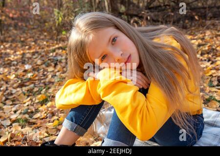 Bella ragazza bionda teen in una felpa arancione brillante e jeans in un parco autunnale. Ritratto d'autunno nella foresta sullo sfondo di caduto l Foto Stock