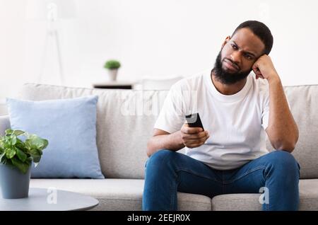 Annoiato guy afroamericano che guarda il programma noioso della televisione a casa Foto Stock