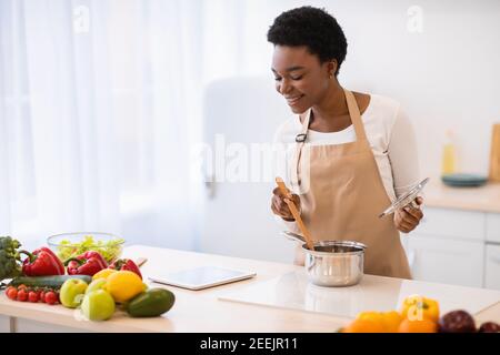 Black Housewife Cooking Browsing Recipes Online via Tablet in cucina Foto Stock