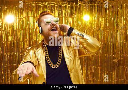 Happy DJ con giacca dorata lucida, cuffie e occhiali da sole fresco che suona musica forte Foto Stock