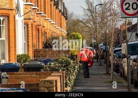 Londra- Postman su strada residenziale di case a schiera a Northfields, Ealing West London Foto Stock