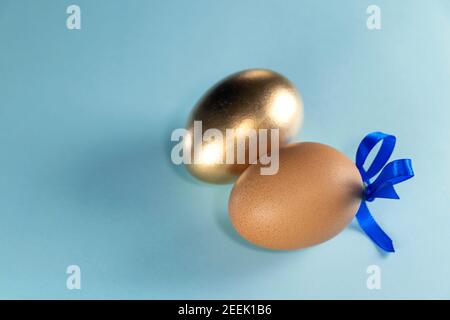 Far rosolare l'uovo con il nastro blu e l'uovo dorato. Buon concetto di Pasqua. Due uova con nastro su sfondo blu pastello con spazio per la copia. Foto Stock