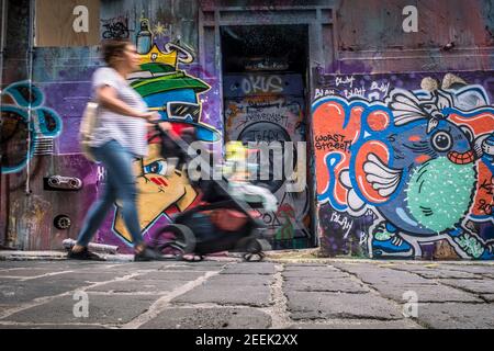 Una donna con un bambino in una sedia a rotelle passa accanto a opere d'arte graffiti su Hosier Street a Melbourne, Australia Foto Stock