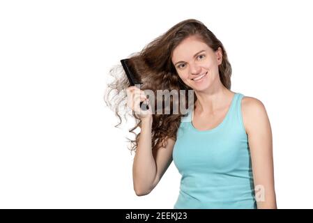 Bella bruna ragazza pettinare capelli ricci lunghi con un pettine e sorridendo su uno sfondo bianco Foto Stock