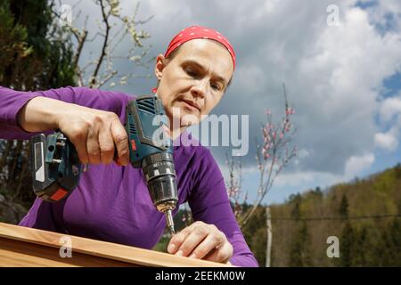 Donna che si avvita un telaio di legno con un trapano elettrico. Concetto DIY. Donna potente. Foto Stock