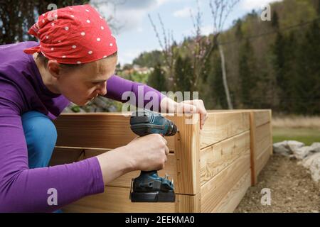Donna che si avvita un telaio di legno con un trapano elettrico. Concetto DIY. Donna potente. Foto Stock