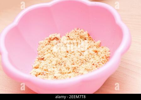 Impasto composto da biscotto tritato e mascarpone per le torte del bambino in un recipiente di plastica rosa Foto Stock