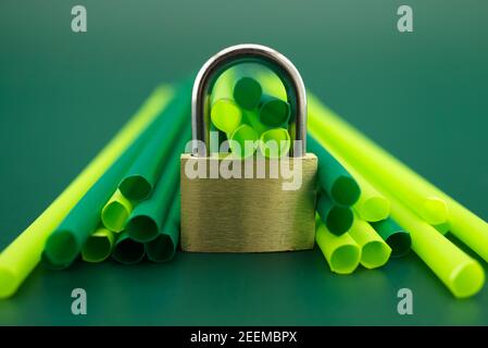 Lucchetto d'oro di fronte a cannucce di plastica per bevande su sfondo verde. Inizio del divieto di utilizzare il concetto di cannucce da bere in plastica Foto Stock